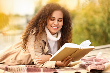 Obraz premium Happy African-American woman reading book on sunny autumn day