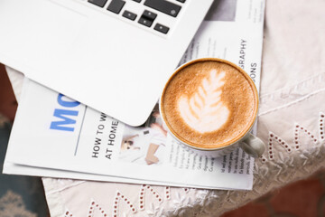 Cup of tasty coffee laptop and newspaper on table in cafe