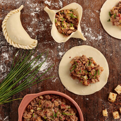Top view of preparation of empanadas with meat filling and potatoes with cibulet. On a rustic wooden table.