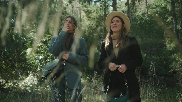 two beautiful women models laughing before posing for camera wearing trendy suits in a forest.
