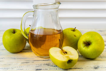 Green apples and jug with apple juice on wooden background
