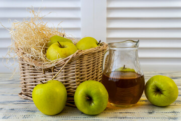 Green apples, basket with apples and jug with apple juice on wooden background