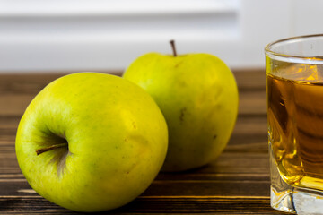 Green apples and glass with apple juice on wooden background