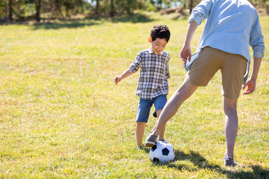 Happy father and son playing football in park - Powered by Adobe