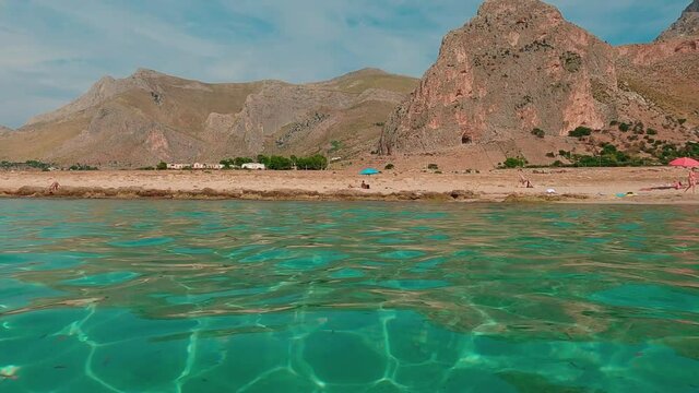 Hot summer day at Baia Santa Margherita and surrounding landscape in Sicily with people bathing in turquoise sea water. Slow-motion tilt-up
