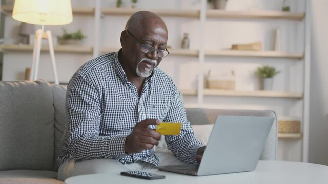 Online banking concept. Senior african american man typing credit card information on laptop at home, slow motion