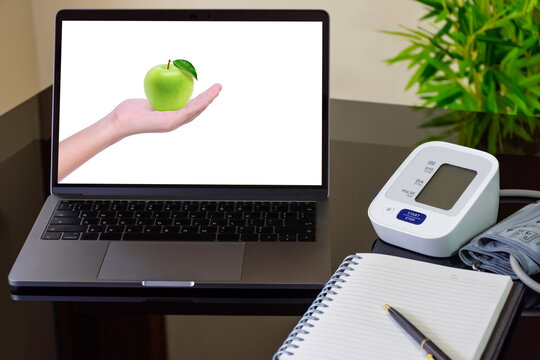 Mockup Laptop Computer With Female Hand Hold Green Apple On Screen With Digital Blood Pressure Guage (sphygmomanometer) And Diary Notebook On The Office Desk