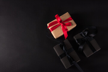 Black Friday Sale shopping concept, Top view of gift box wrapped black paper and black bow ribbon present around the brown box with red bow ribbon, studio shot on dark background