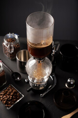 Vacuum coffee maker also known as vac pot, siphon or syphon coffee maker and toasted coffee beans on rustic black stone table.
