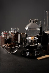 Fototapeta na wymiar Vacuum coffee maker also known as vac pot, siphon or syphon coffee maker and toasted coffee beans on rustic black stone table. Copy space for your text