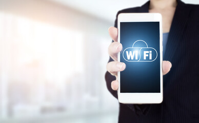 Wi Fi wireless concept. Hand hold white smartphone with digital hologram Wi Fi sign on light blurred background. Free WiFi network signal technology internet concept.
