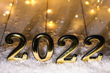 Gold numbers 2022 on wood background with snow and luminous garland. New year backdrop with 2022 year