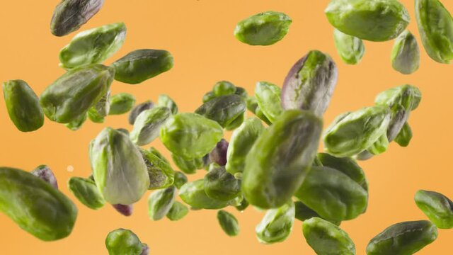 Flying of Peeled Pistachios in Pale Orange Background