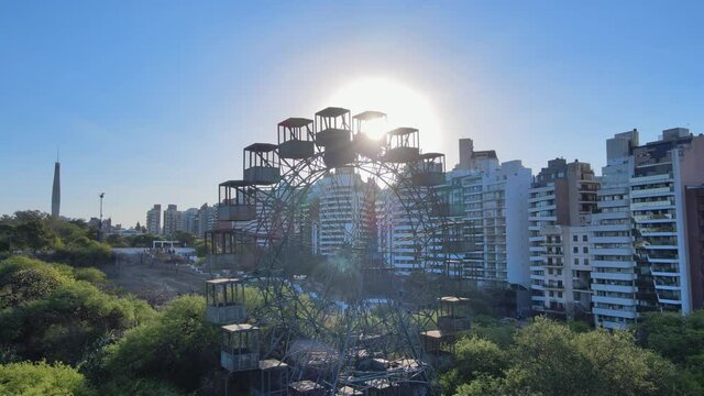 Cinematic aerial pan shot capturing old vintage dysfunctional Rueda Eiffel ferris wheel with sunlight peaking through the iron structure.