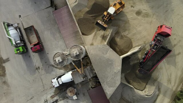 Aerial top down view of an excavator and a dump trucks in a concrete factory construction site