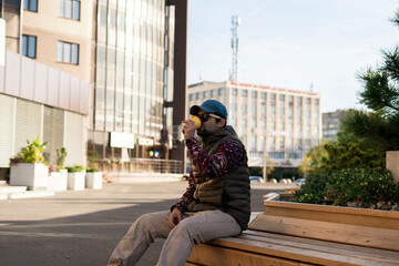 young bearded man in sunglasses drinking takeaway coffee walking outdoors