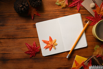 Top view empty notebook, coffee cup and maple leaves on wooden background.