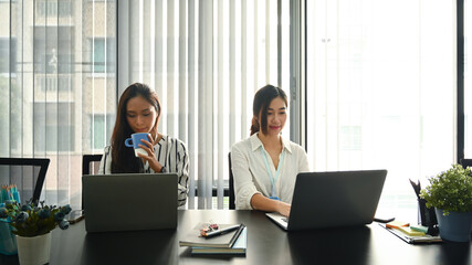 Two asian women colleagues sitting together in office.