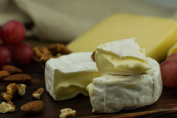 Camembert cheese with white mold with a soft cream piece on it. against the background of nuts and grapes.