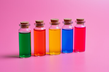 Colored liquids in transparent bottles with a wooden stopper on a pink background