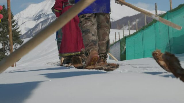 Men dressed in traditional deel walking in ancient fur ski in snow. Close up low angle. Bright winter day Hemu Village, Xinjiang, China. 