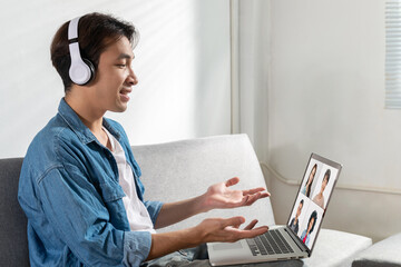 A student with headphones on is explaining while holding a laptop and watching video call....