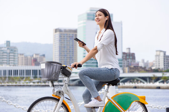 Smiling girl in headphones, holding smartphone and riding bicycle in the park - Powered by Adobe