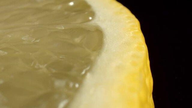 Macro shot of a slice of yellow lemon on the black background. Pulp of citrus lemon, close-up. The use of lemon in cosmetology. High quality. 4k footage.