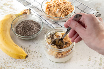 Person eating a jar full of cereal, greek yogurt, bananas and crisps with a spoon A healthy organic breakfast in the morning.