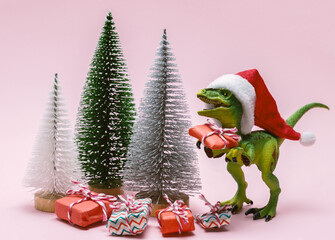 Funny plastic toy dinosaur wearing Santa Claus hat with  present boxes on a pink background.