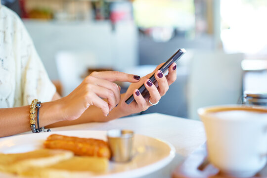 Woman holding mobile phone in hands, texting in social media. Breakfast of business lady.