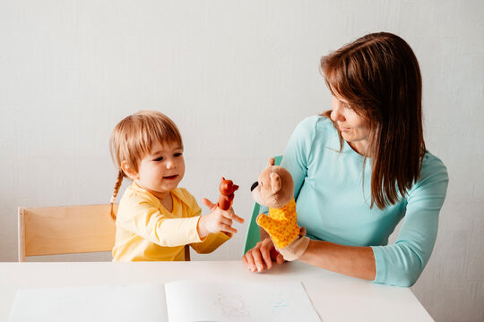 Mother and  little daughter are sitting at  table and playing finger theater against white wall. Family together, learning through game concept.