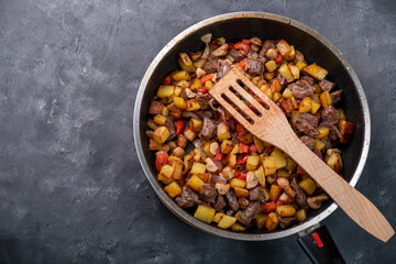 Fried potatoes until golden brown with pieces of meat and mushrooms in a pan. Top view, free space.