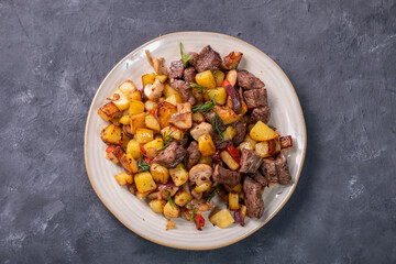 A plate of fried potatoes with a golden, appetizing crust, mushrooms and pieces of meat. Top view.