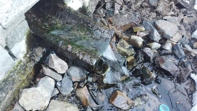 Steadicam shot of winter gushing spring out of a brick wall by granite gutter and falling on rocks. Some ice also