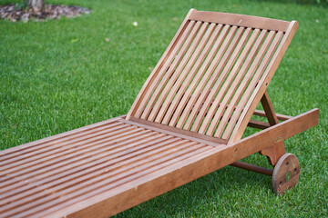 Close-up of a wooden chaise longue in a fresh garden on green grass.The concept of relaxation, tanning in the backyard. High quality photo