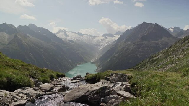 There is a litte stream flowing in the foreground and the Austrian alps, as well as a beautiful blue lake in the background.