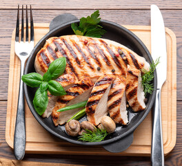 Roasted chicken fillet and mushrooms with herb in the frying pan on the wooden table close-up.