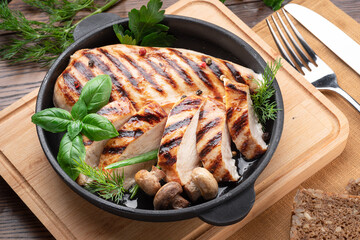 Roasted chicken fillet and mushrooms with herb in the frying pan on the wooden table close-up.