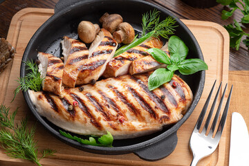 Roasted chicken fillet and mushrooms with herb in the frying pan on the wooden table close-up.