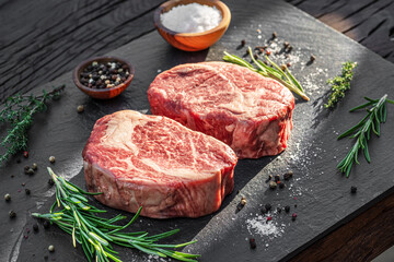 Raw Ribeye steaks with salt and herbs on grey board. Top view.
