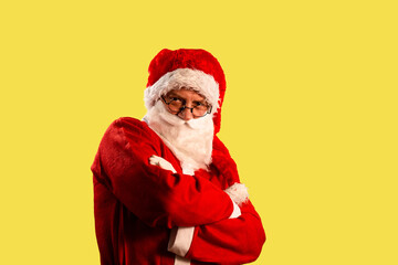 Fototapeta na wymiar Santa Claus wearing round eyeglasses with crossed arms looking serious and influential directly in a camera; isolated portrait on yellow background.