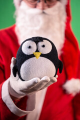Santa Claus wearing red coat and white gloves, holding a cute penguin toy in his hand