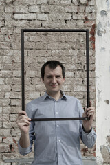 young man on the background of a brick wall holding a wooden photo frame in his hands © andreysafonov