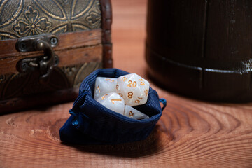 A set of white polyhedral cubes for role-playing games lie in a blue storage bag next to a wooden box and a mug: the concept of board games