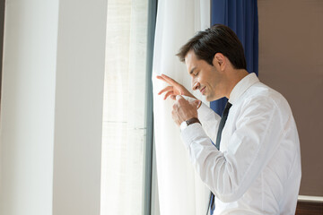 Fototapeta premium Handsome young businessman drinks coffee in front of the hotel window