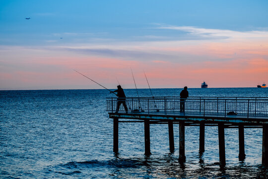 Fototapeta People fishing on the pier at sunset
