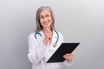Photo of happy dreamy lady doctor wear white coat spectacles smiling signing documents looking empty space isolated grey color background
