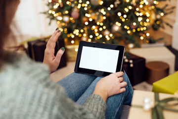 concept of christmas, technology and winter holidays - close-up of woman with digital tablet at home against the background of a Christmas tree is greeted by video call. online communication