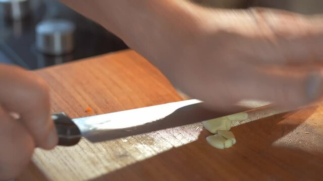 Minced garlic, close-up of the process of chopping garlic on a wooden cutting board. Healthy eating. Selective focus. The chef cuts vegetables with a knife